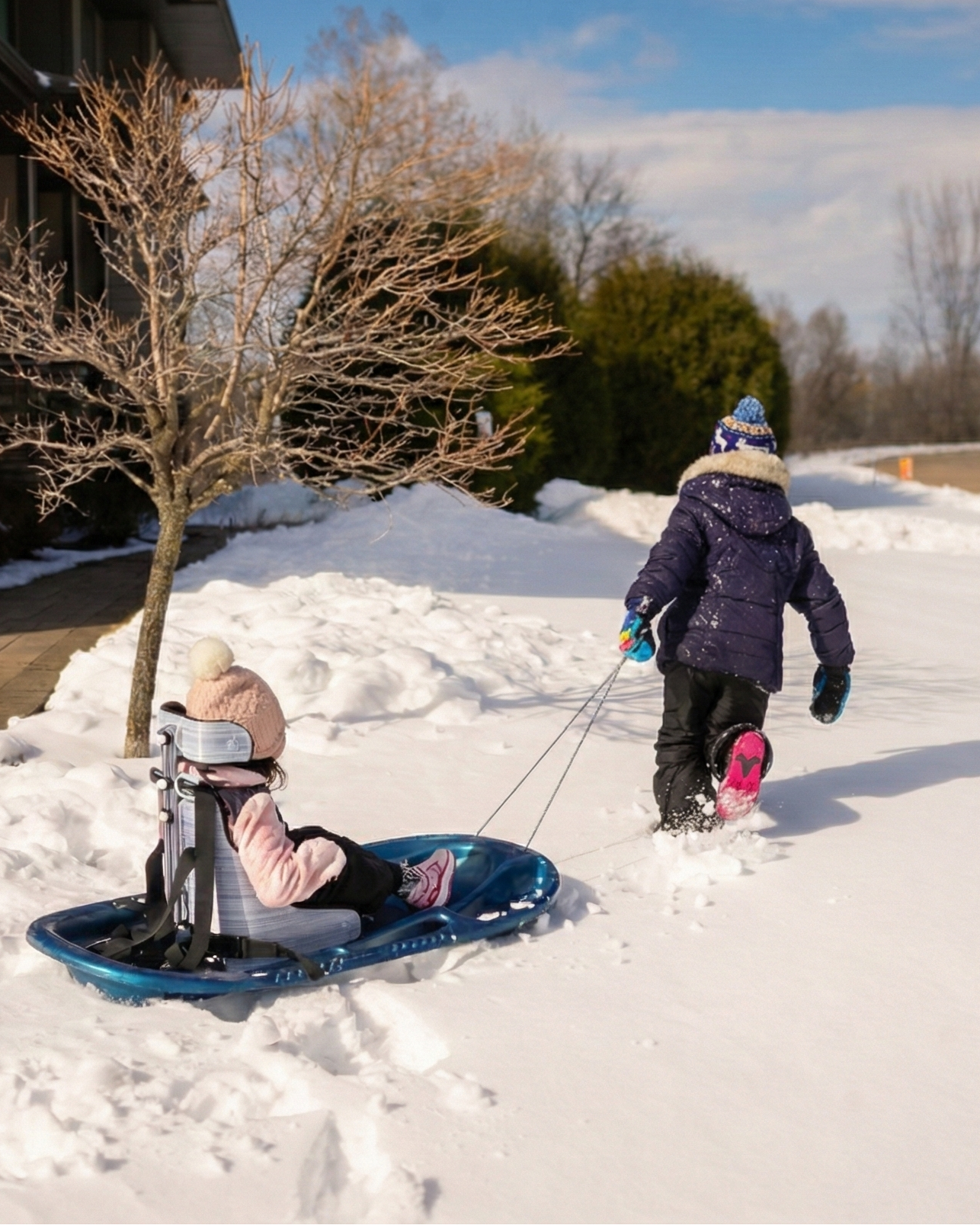 Two children playing in the snow with a sled with testa-seat on a residential street